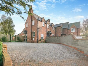 A large brick house with a gravel driveway and a stone wall.