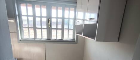 A small, enclosed room with a window, tiled floor, and a trash bin.