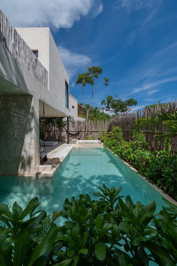 Una casa moderna con piscina, rodeada de exuberante vegetación y un cerco de madera.