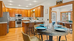 Una cocina moderna con armarios de madera, electrodomésticos de acero inoxidable y una zona de comedor con platos y sillas azules.
