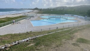 Un área de piscina con varias piscinas, una playa al fondo y un paisaje montañoso.