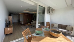 Una sala de estar moderna con una mesa de comedor de madera, sillas y un sofá. Hay una puerta corrediza de vidrio que da a un balcón.