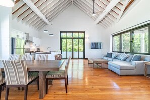 A spacious interior with a dining area, kitchen, and seating area, featuring a high ceiling and large windows.