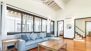 Una sala de estar moderna con sofá, mesa de centro y mesitas auxiliares. Amplios ventanales dejan entrar luz natural y ofrecen vistas al exterior.