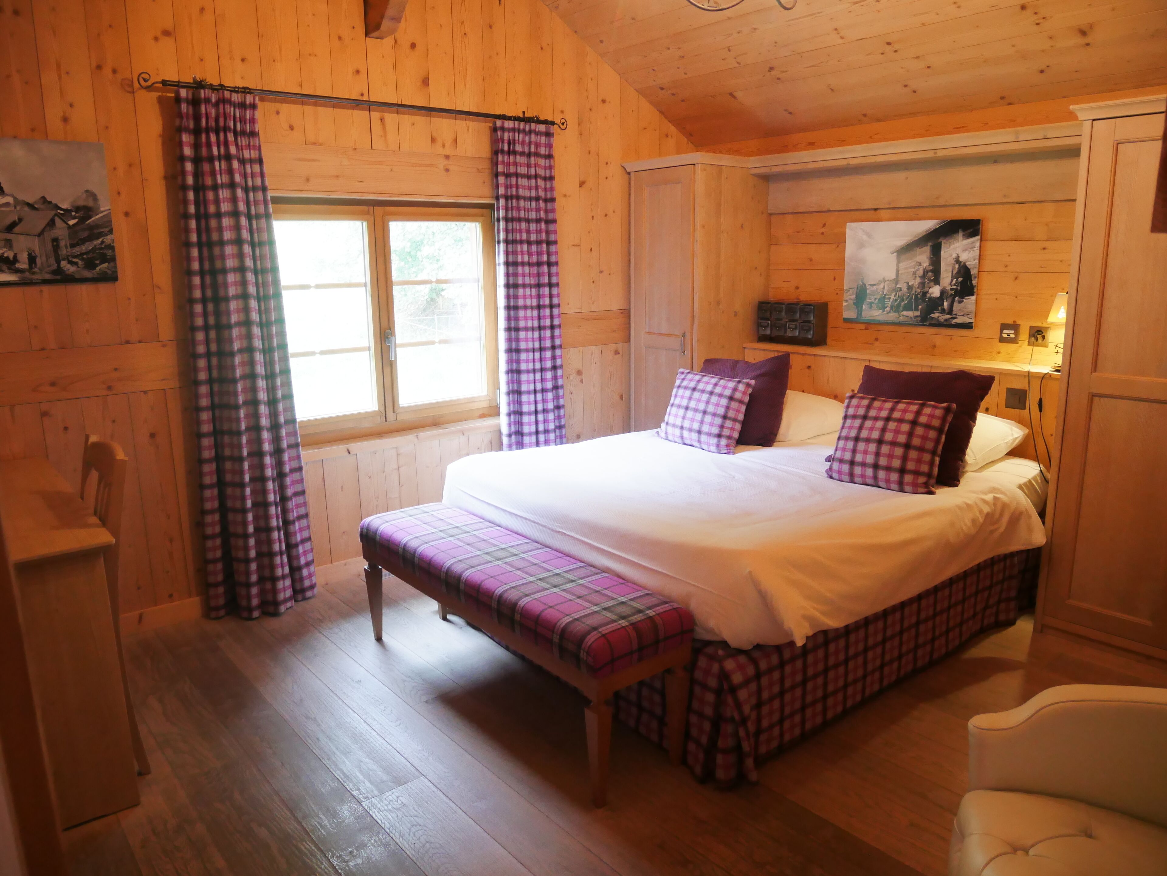 Ein Schlafzimmer einer Holzhütte mit Bett, Sitzbank und Vorhängen.