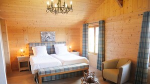 A cozy room with a wooden ceiling, a bed with plaid bedding, a chair, a small table with a decorative item, and a painting on the wall. - Between Boutique Hotel (Chamoson)