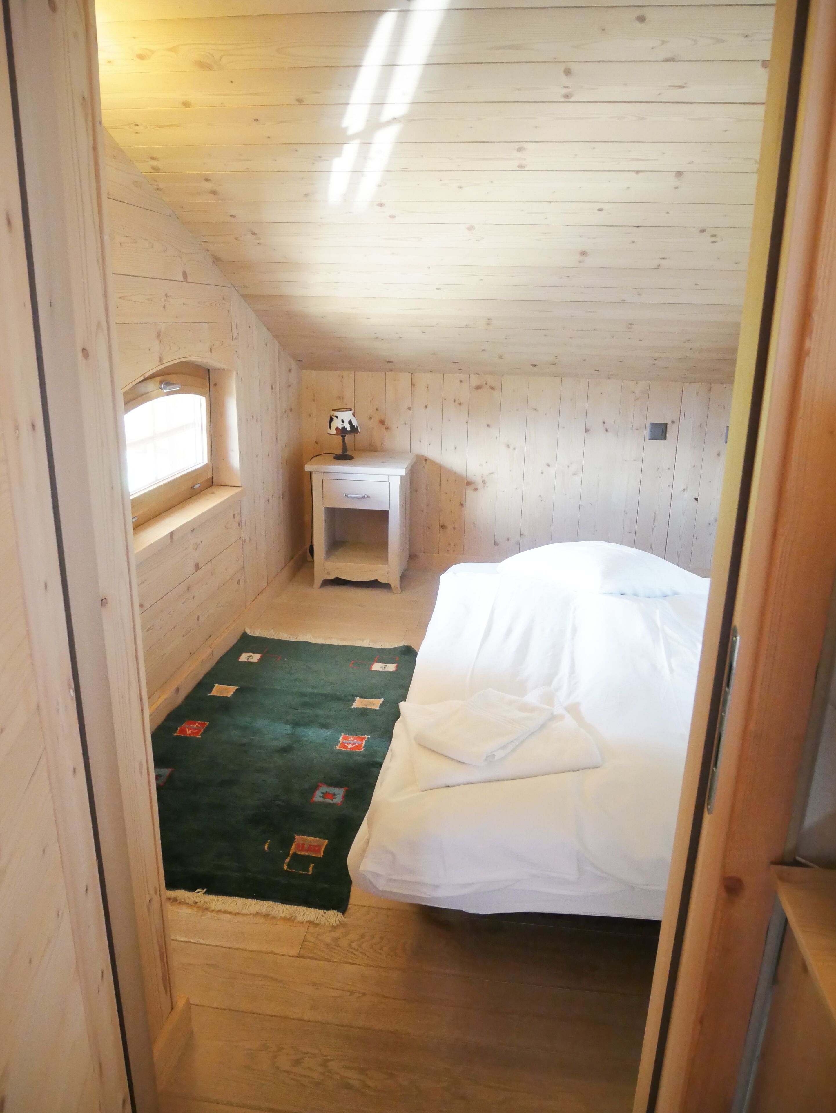 Una habitación pequeña con paneles de madera, una cama individual, una mesita de noche y una ventana.