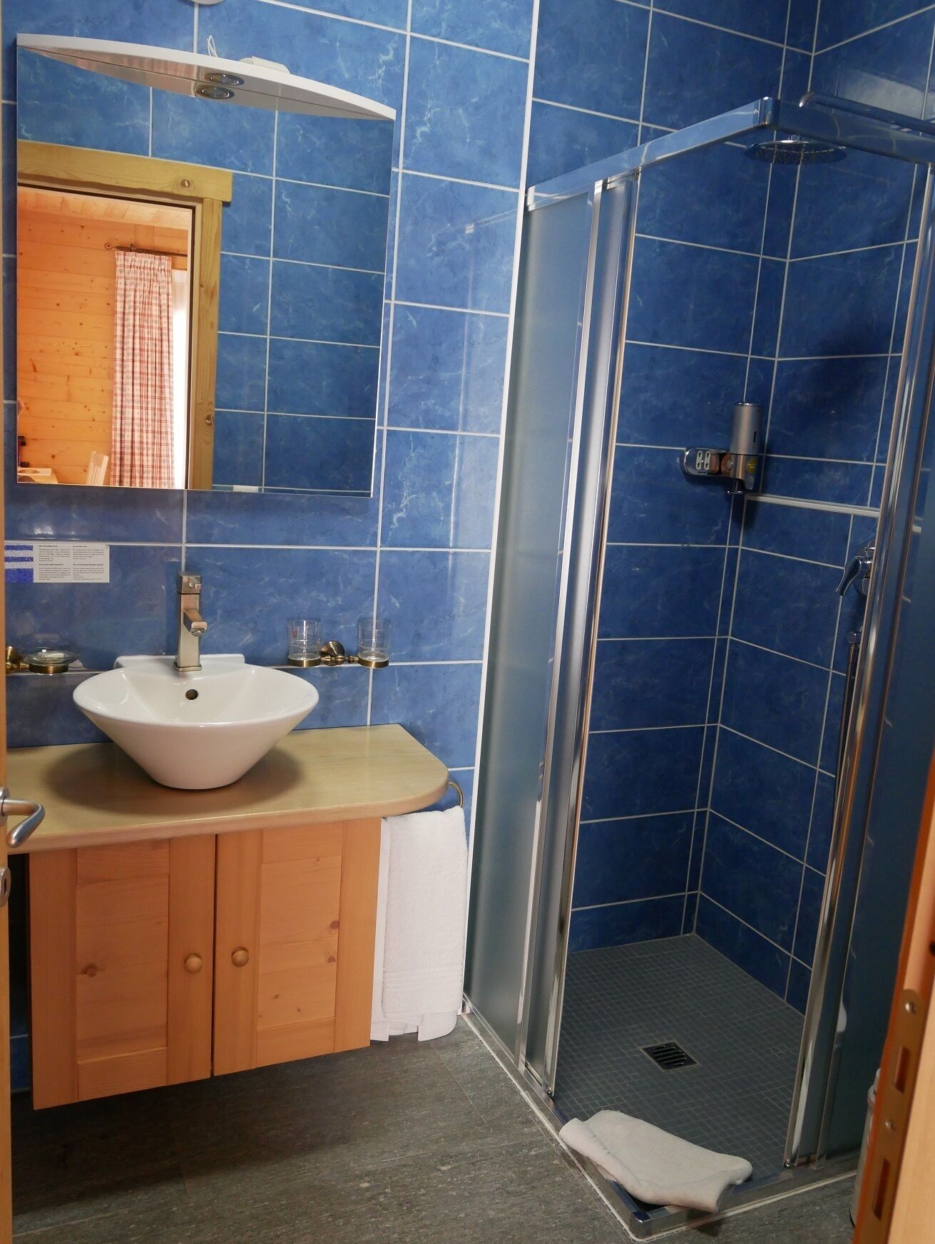 A bathroom with a white sink, wooden cabinets, a mirror, and a blue-tiled shower area.