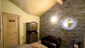 A cozy room with a stone wall, a wooden ceiling, a brown leather sofa, a wooden cabinet, and a small table. - Between Boutique Hotel (Chamoson)