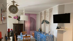 Un comedor con una mesa, sillas, un armario azul, un reloj y un televisor montado en la pared.