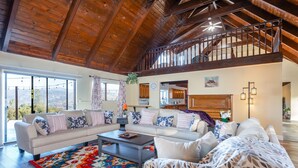 A spacious living room with a high ceiling and exposed wooden beams, a large sofa set, a coffee table, and a colorful rug. - New!! Majestic Views, Pool, Sleeps 20+, 2 Mstr BR, close DT Yosemite, Bass Lake  (Oakhurst)