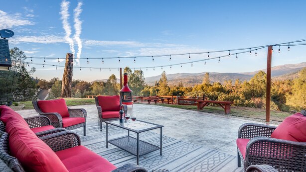 An outdoor patio area with wicker furniture and red cushions, a glass-top coffee table, and a view of the surrounding landscape. - New!! Majestic Views, Pool, Sleeps 20+, 2 Mstr BR, close DT Yosemite, Bass Lake  (Oakhurst)