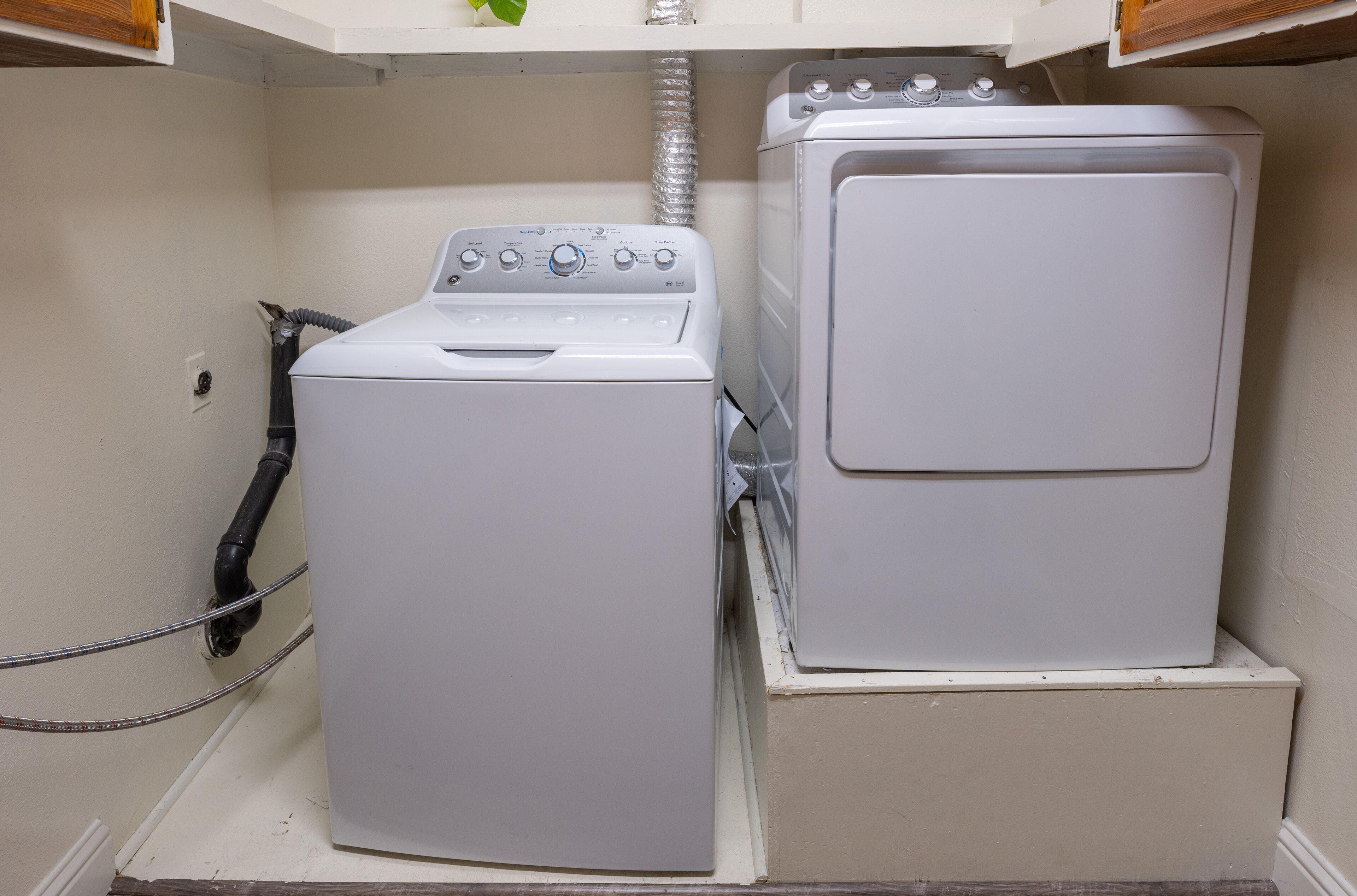 A compact laundry area with a front-loading washer and dryer, a visible power outlet, and a flexible hose.