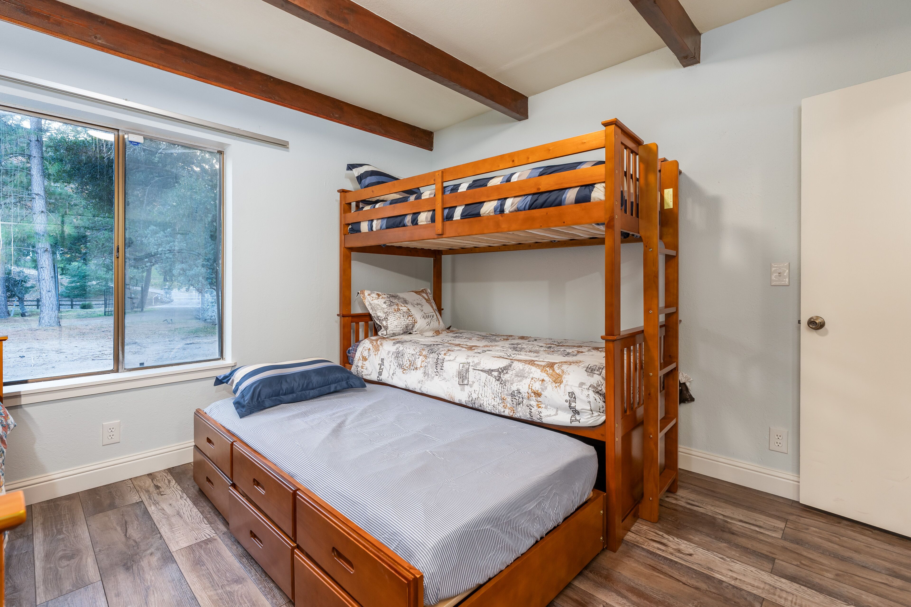 A bunk bed room with a window, wooden floor, and a door.