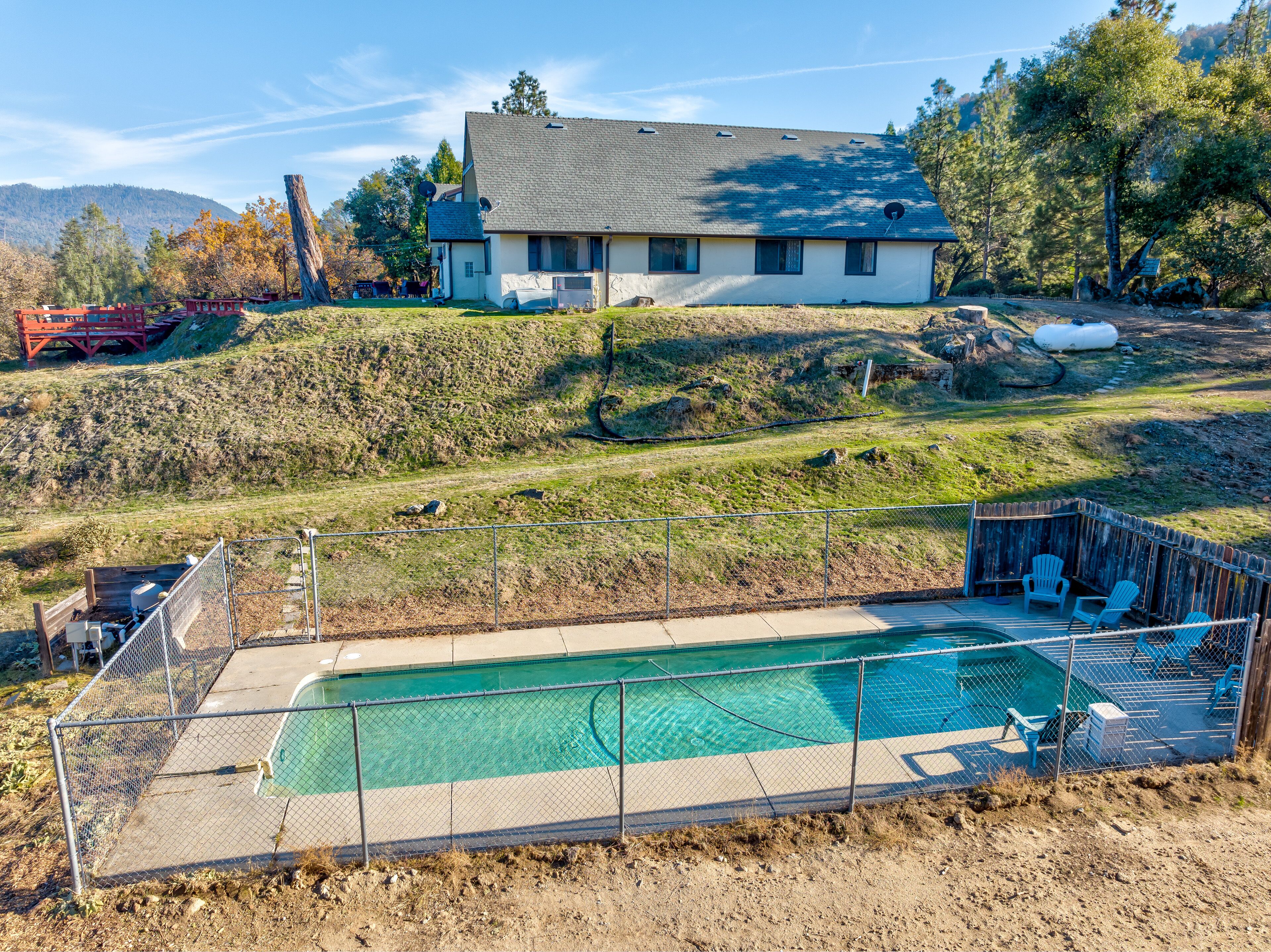 A house with a swimming pool, surrounded by a fenced yard and a hilly landscape.