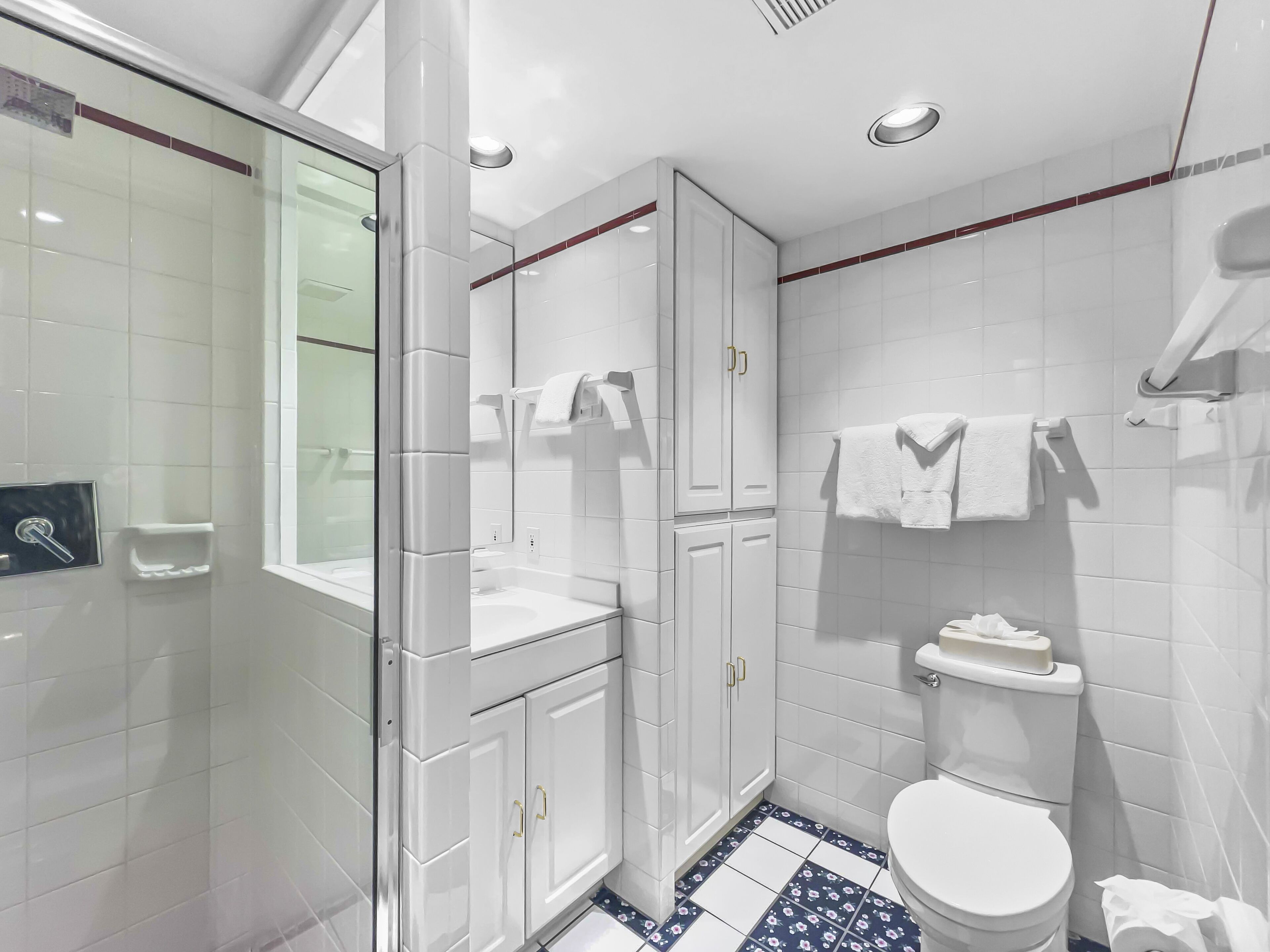 A modern bathroom with white tiles, a glass shower enclosure, a white toilet, and a sink with a mirror.