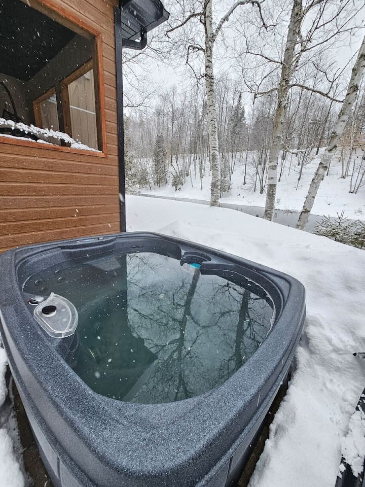 Soak in the private hot tub as snow falls over the riverside woods.