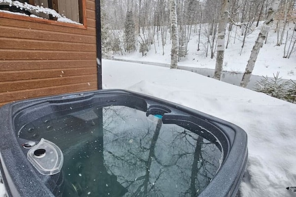 Soak in the private hot tub as snow falls over the riverside woods.