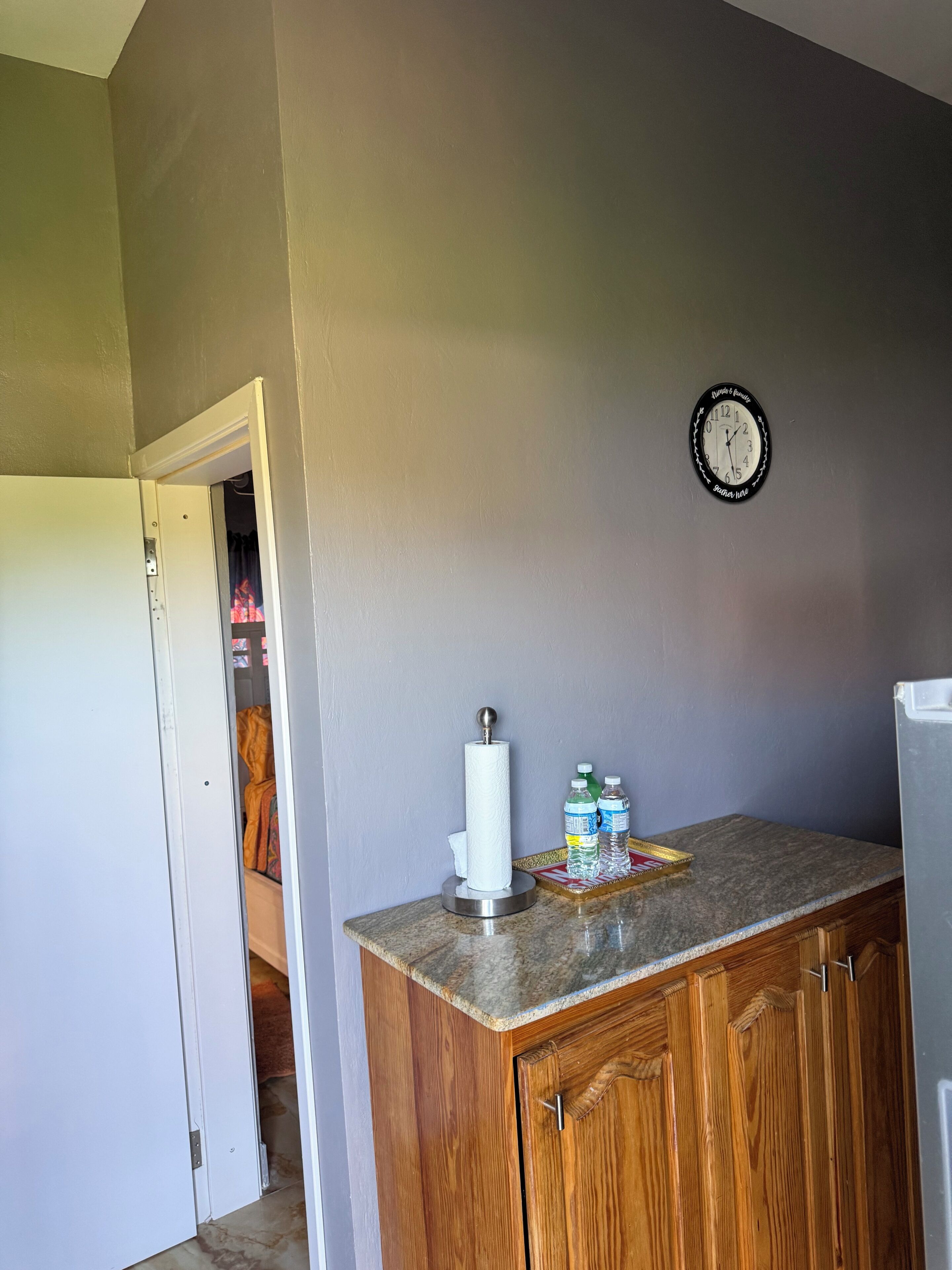 A kitchen with a wooden cabinet, a countertop, a paper towel holder, and a clock on the wall.