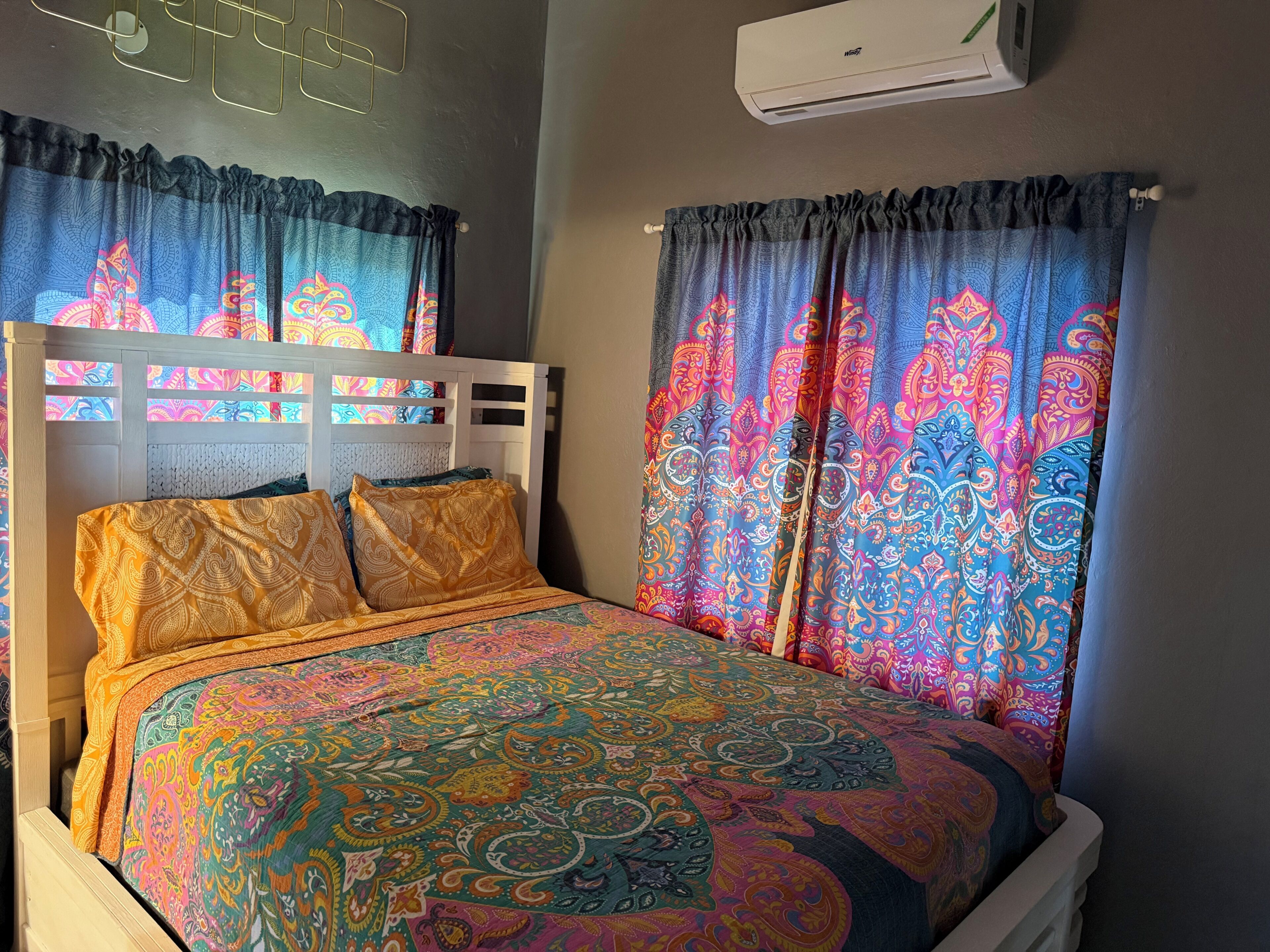 A bed with patterned bedding, a headboard, and curtains with a paisley design.