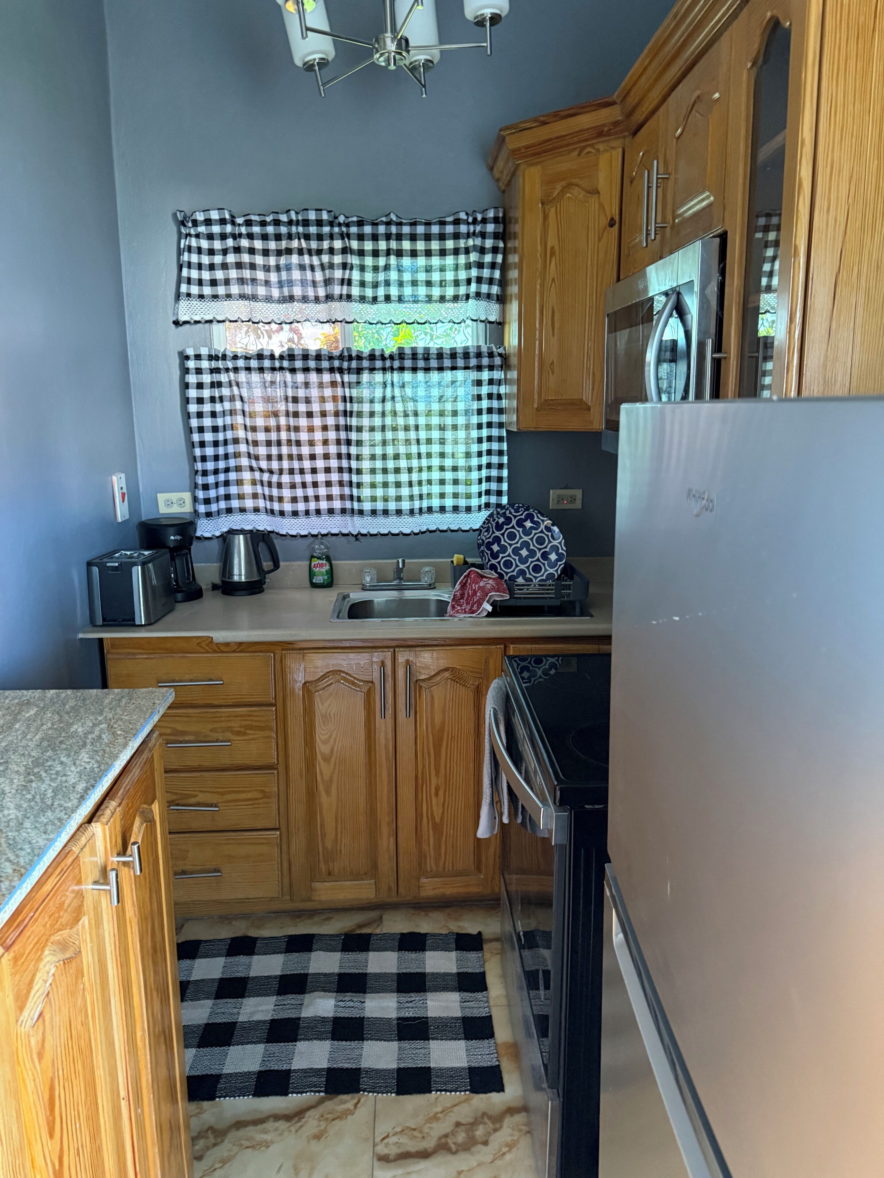 A compact kitchen with wooden cabinets, a stainless steel refrigerator, a microwave, and a coffee maker.