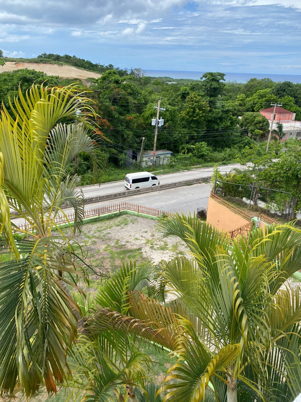 A white van on a road with a red fence and greenery in the foreground.