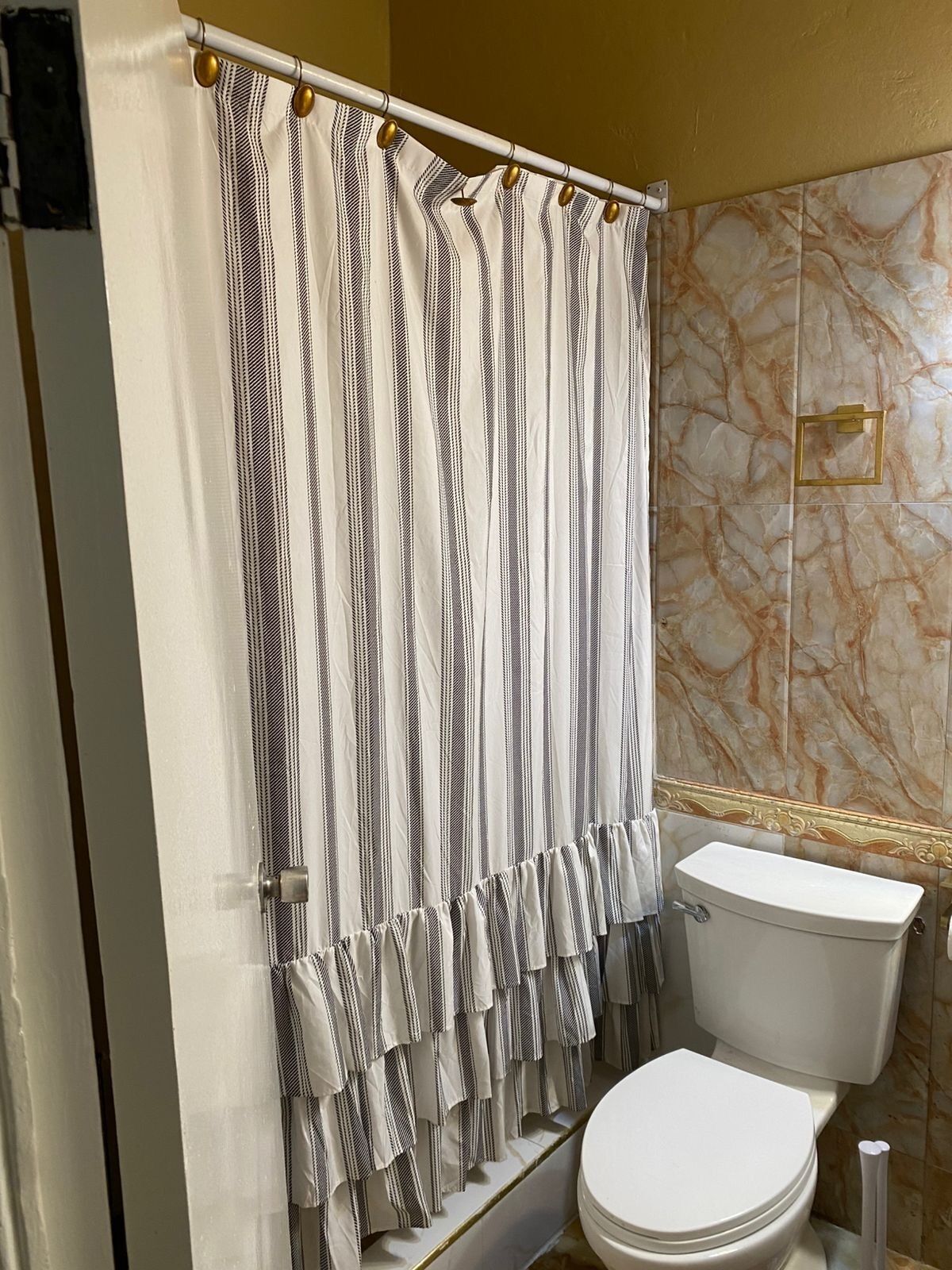 A bathroom with a striped shower curtain, a toilet, and marble-patterned walls.