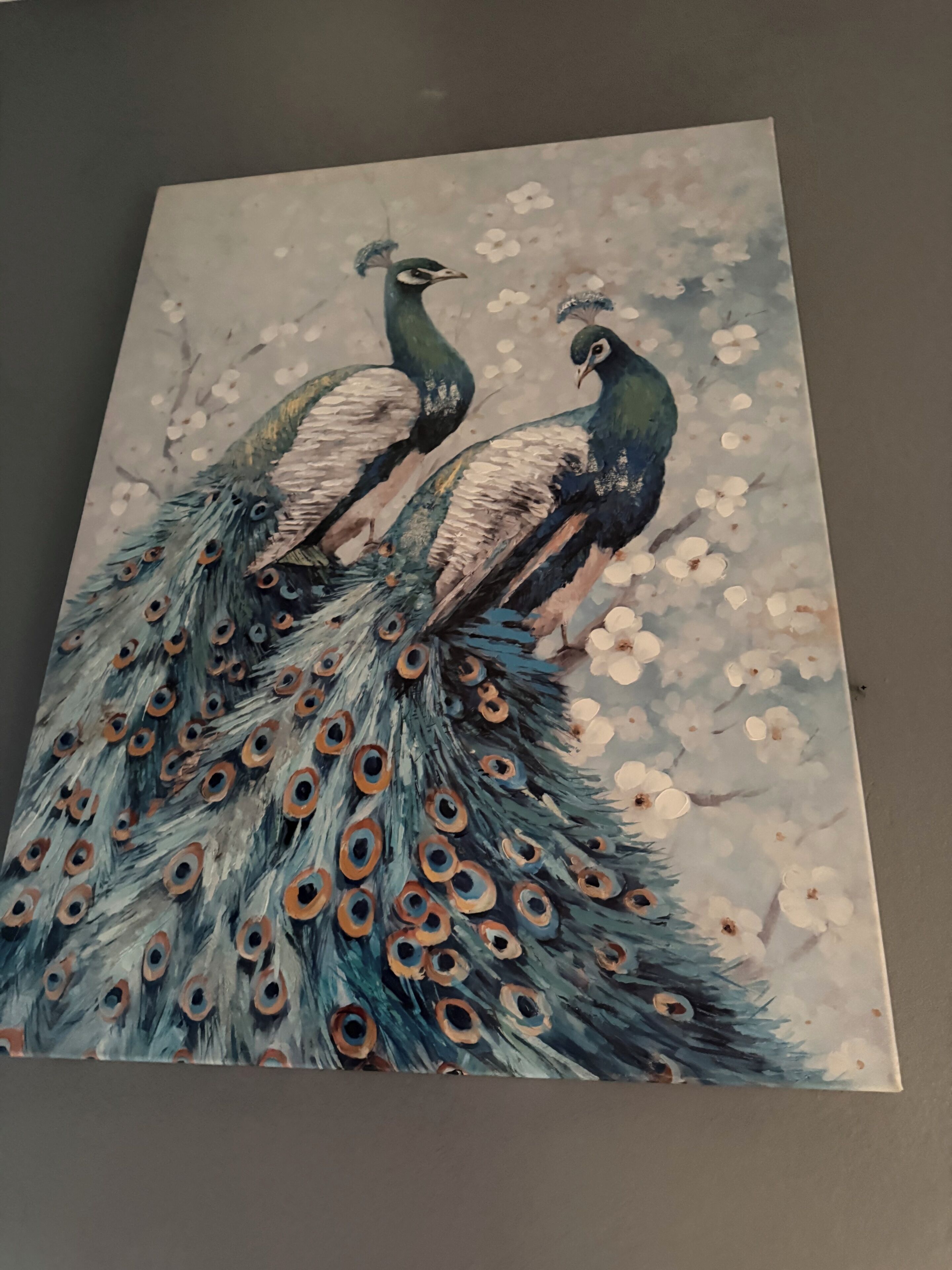 Un tableau représentant deux paons aux plumes détaillées, sur un fond floral.