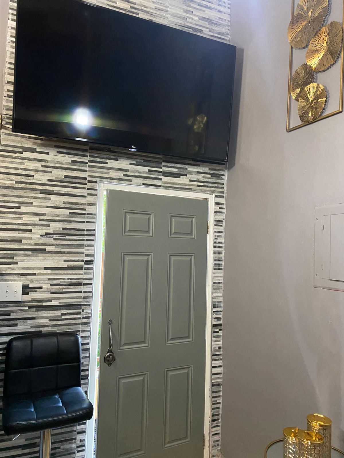 A room with a flat-screen TV mounted above a door, a patterned wall, a black chair, and a decorative wall piece.