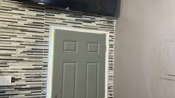 A room with a flat-screen TV mounted above a door, a patterned wall, a black chair, and a decorative wall piece.