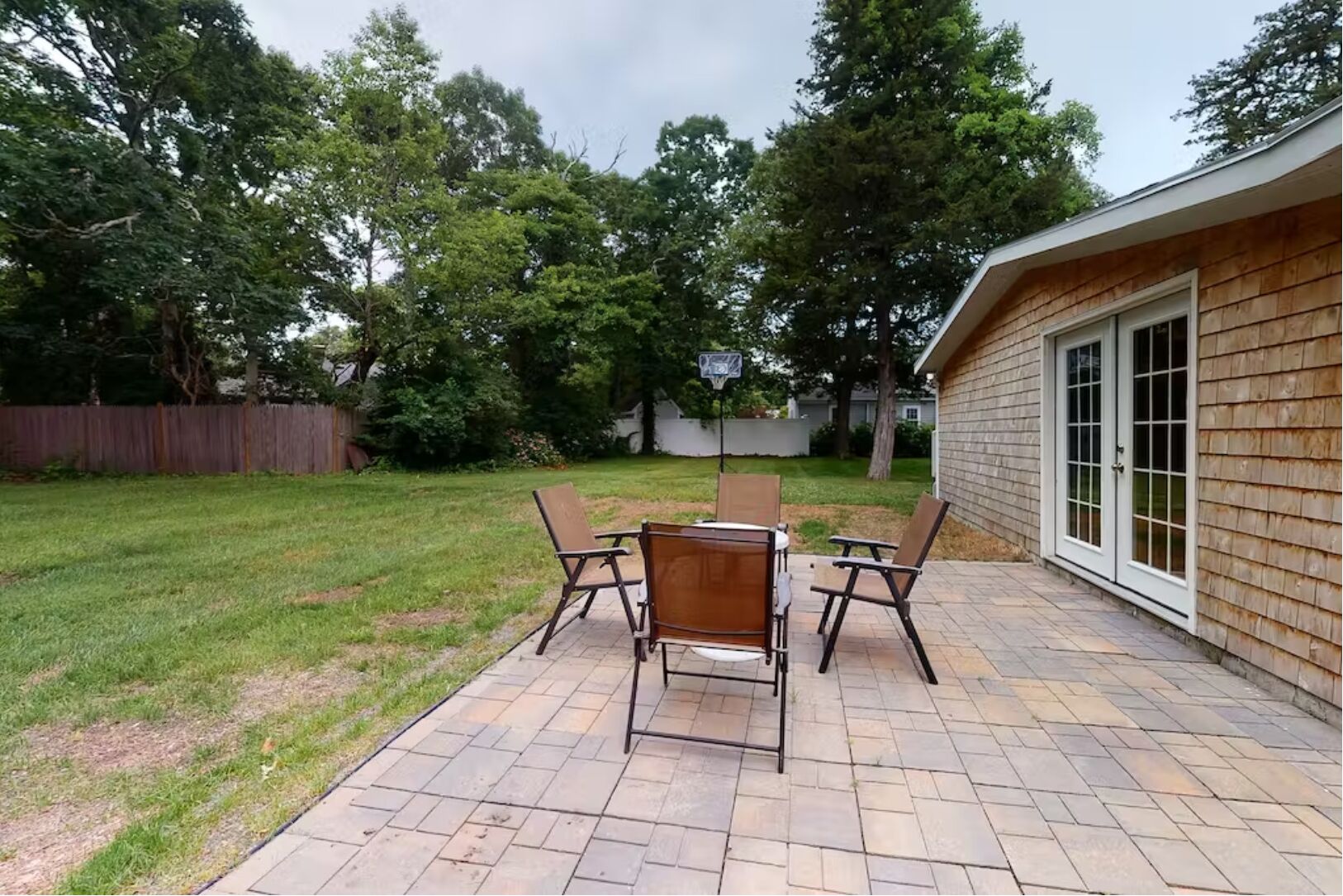 Une terrasse avec une table et des chaises, un panier de basketball et une clôture en bois.