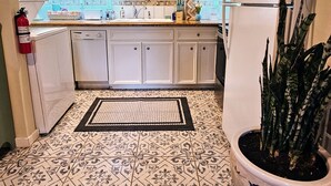 A kitchen with white cabinets, a white refrigerator, a sink, and a potted plant.