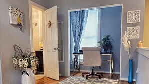 A hallway with wooden flooring, a white door, a blue curtain, and a small table with a chair.