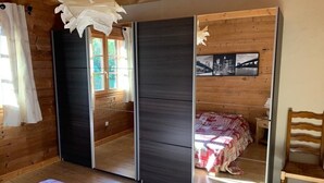 Una habitación con paredes de madera, una cama con colcha estampada, una silla y un estante con una foto enmarcada.