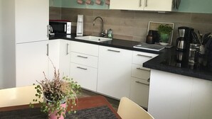 Et moderne køkken med lyse skabe, en sort bordplade, en vask, en kaffemaskine og en potteplante.