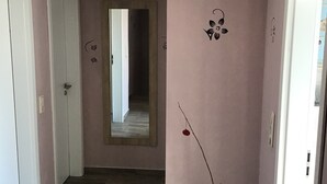 En gang med trægulv, et stort spejl på væggen og en grøn vase.