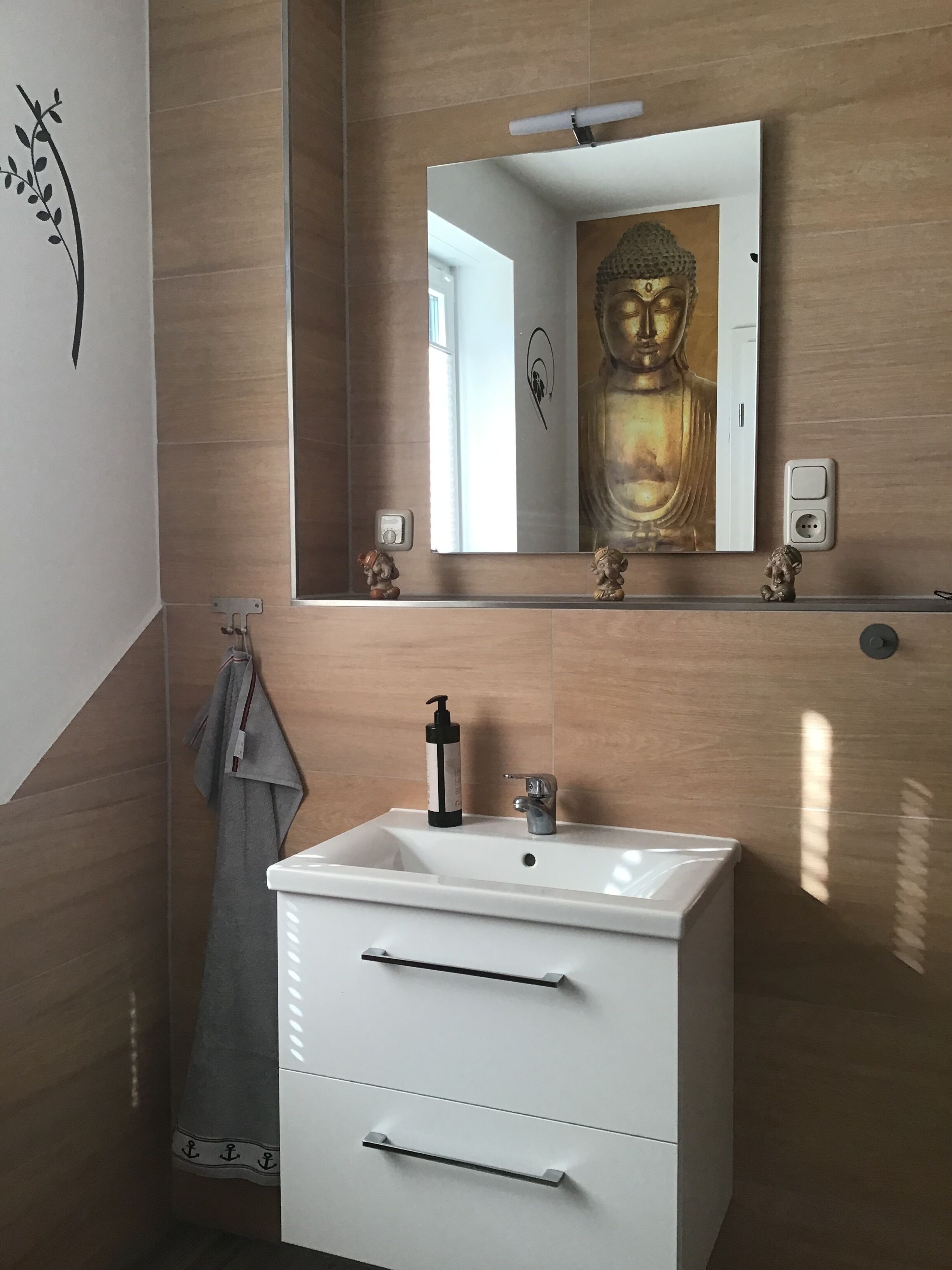 Un baño con un lavamanos blanco, un espejo y una estatua de Buda.