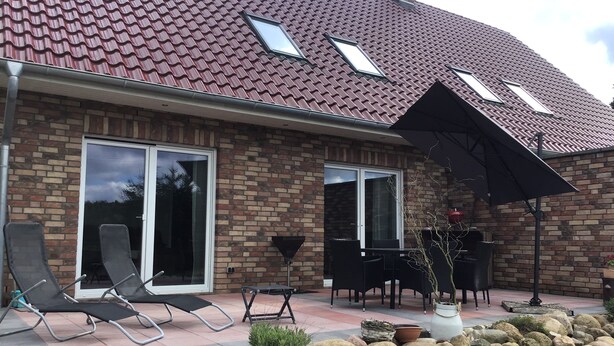 Et hus med røde teglsten, murstensfacade og en terrasse med udendørs møbler.