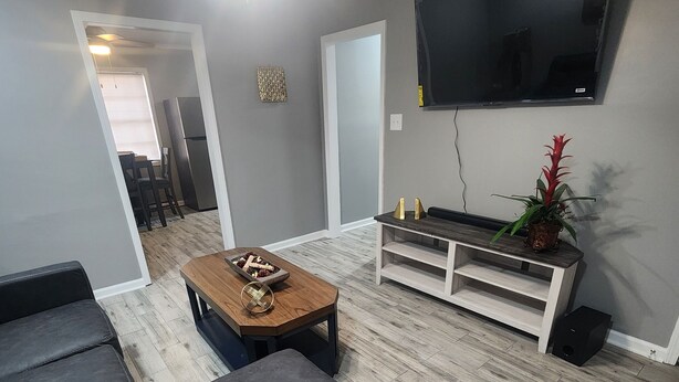 Un salon moderne avec un canapé gris, une table basse en bois et un téléviseur à écran plat fixé au mur.