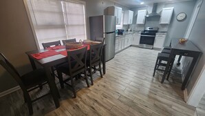 Une cuisine moderne avec des meubles blancs, un réfrigérateur en acier inoxydable et un four à micro-ondes. On y trouve une table à manger avec des chaises et un set de table rouge.