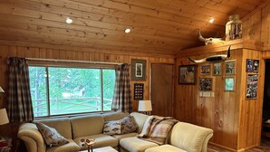 A cozy room with a wooden interior, featuring a sofa set, a coffee table, and a large window with a view of greenery outside. - Cozy Utah Cabin (Kamas)