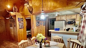 A wooden interior with a dining table, chairs, a chandelier, and a kitchen area. - Cozy Utah Cabin (Kamas)