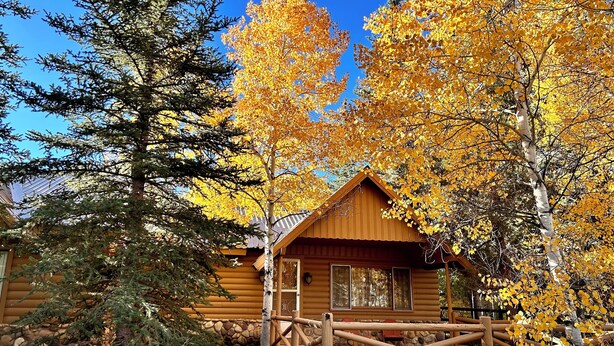 A log cabin with a wooden deck and a stone wall foundation. - Cozy Utah Cabin (Kamas)
