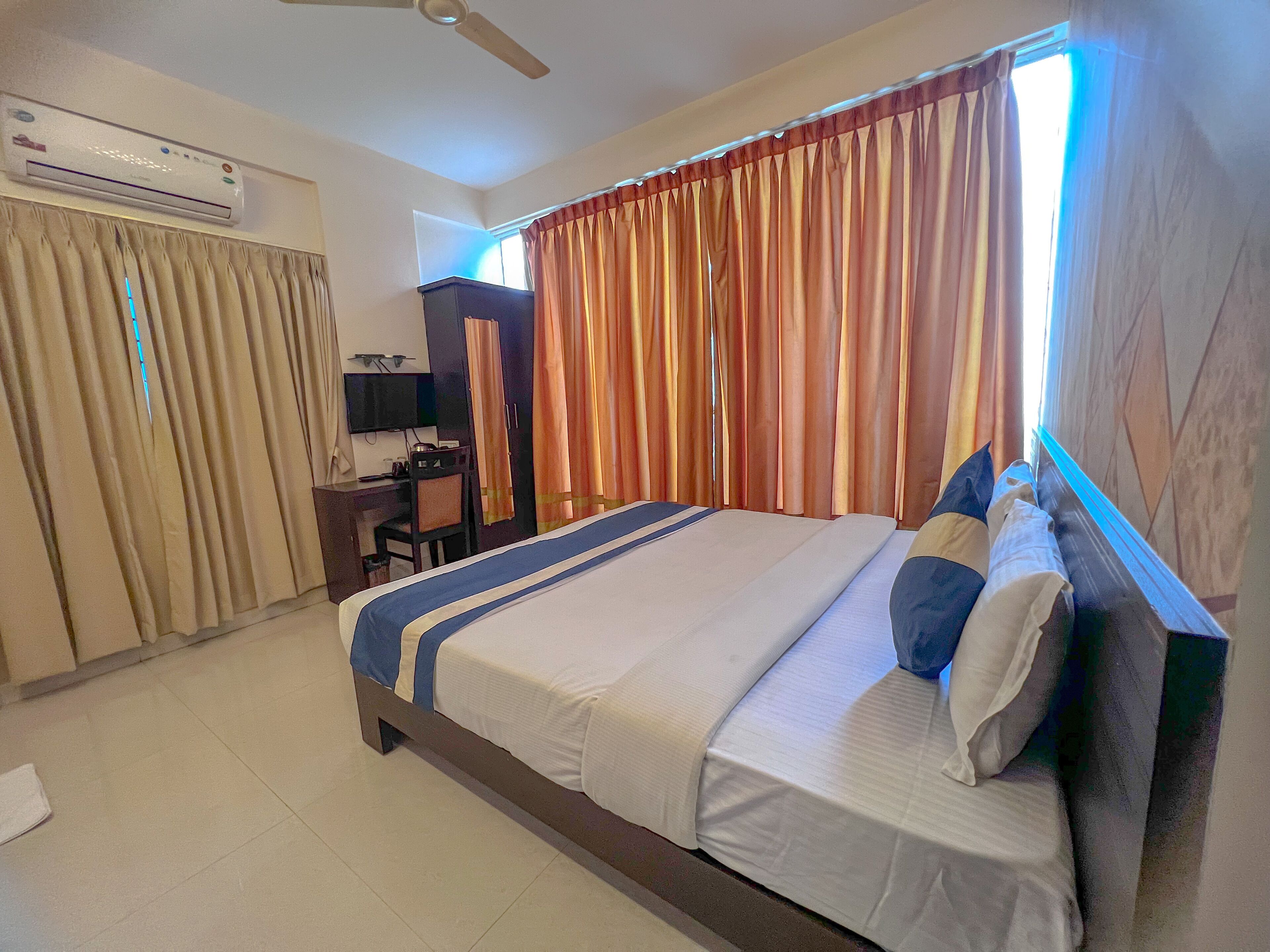 A hotel room with a bed, a desk, a chair, an air conditioner, and curtains.