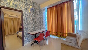 A hotel room with a dining table, red chairs, a sofa, and a window with orange curtains. - Hotel Willow Tree (Bengaluru)