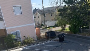 Um estacionamento com vagas demarcadas, uma lixeira e um edifício ao fundo.