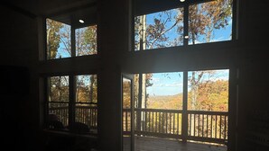 Una habitación con grandes ventanales que dan a una terraza de madera y follaje otoñal.