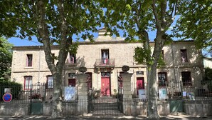 A historic building with a central red door, stone facade, and a sign reading "ECOLES CONHORLES". - L'atelier du Salagou (Octon)