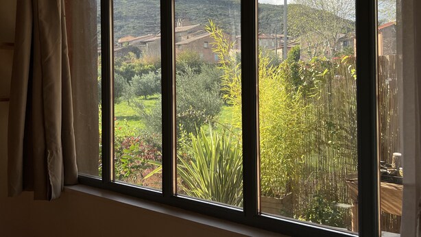 A window with a view of a garden and buildings in the distance. - L'atelier du Salagou (Octon)