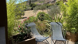 A garden with two chairs, a stone planter, and a view of a hillside with buildings. - L'atelier du Salagou (Octon)